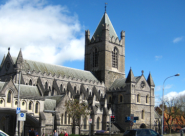 Gothic-style cathedral with a tall, pointed tower under a blue sky with white clouds. The stone building is detailed and imposing, evoking historical grandeur.