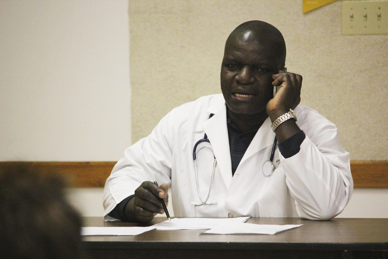 A Kenyan doctor telephones a patient who recently came in for a cancer screening. The sketch shows why calling a patient at work to announce her diagnosis can devastate the patient. It also reveals that physicians from other countries may be looked down upon by colleagues and patients.
